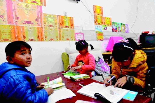 邱梦娜和弟弟妹妹一起写作业,旁边的墙上贴满了邱梦娜获得的奖状